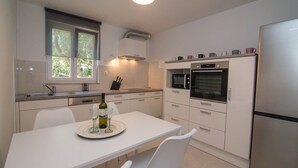 Une cuisine moderne avec des meubles blancs, une table à manger avec des chaises, un réfrigérateur, un four à micro-ondes et un four traditionnel.