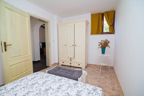 Ein Schlafzimmer mit einem Bett, einem Kleiderschrank, einem kleinen Tisch mit einer Vase und einem Fenster mit Vorhängen.