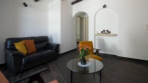 Un salon moderne avec un canapé en cuir noir, un fauteuil jaune et une table basse en verre sur laquelle est posé un vase de fleurs.