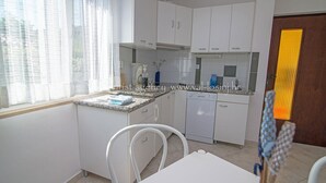 Een kleine keuken met witte kastjes, een vaatwasser en een raam met dunne gordijnen.