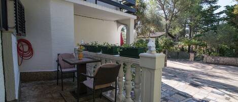 An outdoor patio with a table and chairs, a railing, and potted plants.