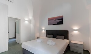 Una camera d'albergo moderna con un letto grande, una testiera, comodini e un quadro raffigurante un tramonto sul mare.