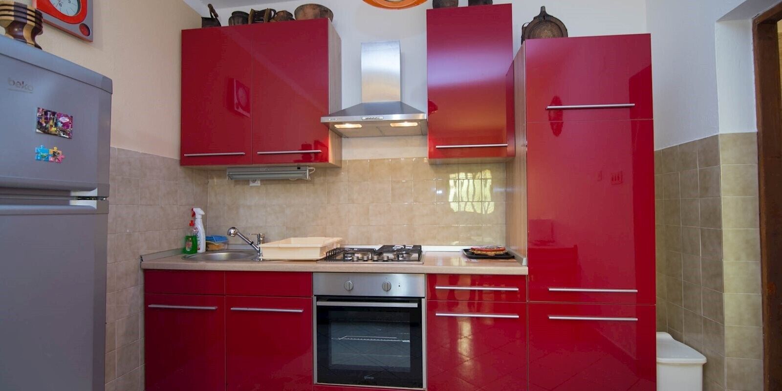 Una cocina compacta con gabinetes rojos, horno integrado y cocina a gas.