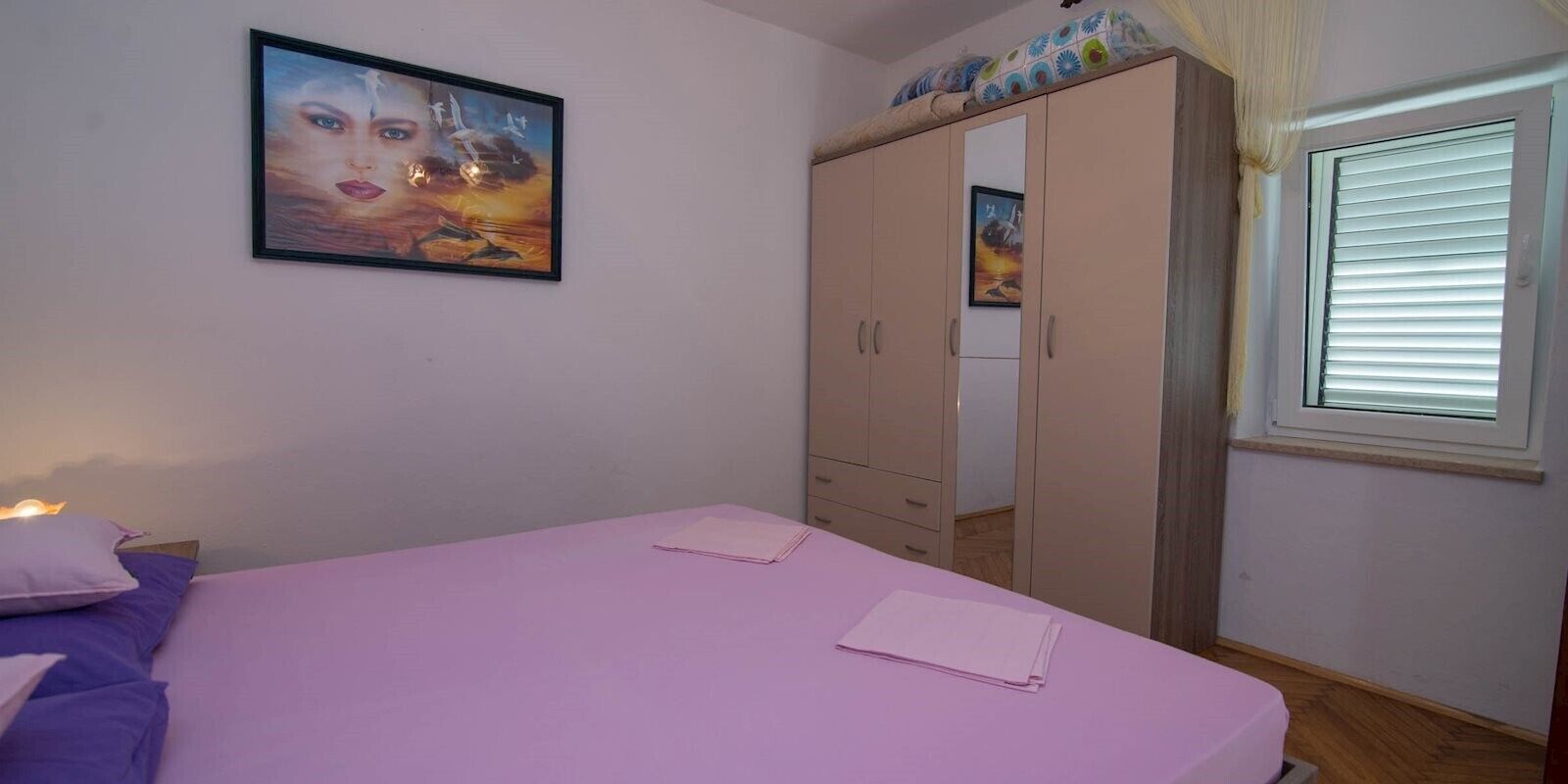 Um quarto com cama, guarda-roupa, janela com persianas e um quadro na parede.
