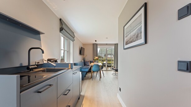 Una cucina moderna con piano cottura integrato, lavello e zona pranzo con una sedia e un tavolo blu.