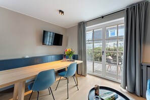 Et moderne spiseområde med et træbord, blå stole, et fladskærms-tv og et stort vindue med gardiner.