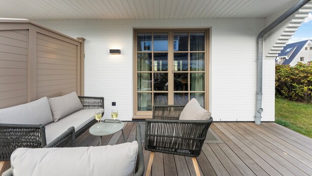 A covered outdoor seating area with wicker furniture and a glass door leading to a room. - Dependance Windrose 174 (Wenningstedt-Braderup (Sylt))