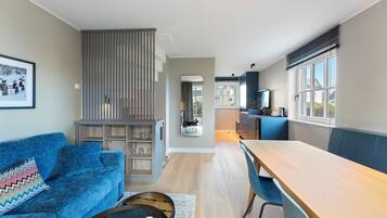Ein modernes Wohnzimmer mit einem blauen Sofa, einem Holzesstisch und einer Küchenzeile mit einem Fenster.