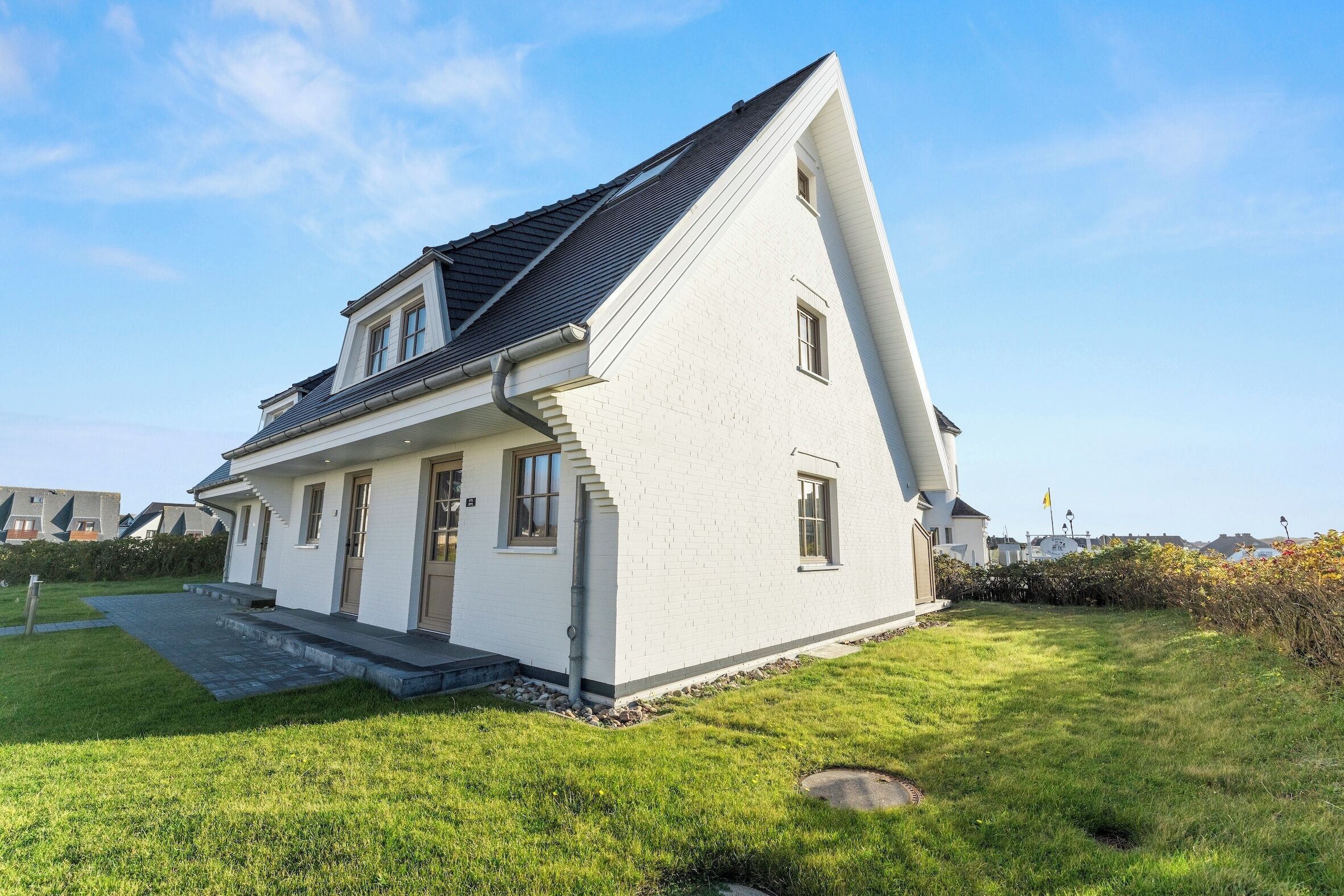 Ett vitt hus med ett sluttande tak, en veranda och en välskött gräsmatta.