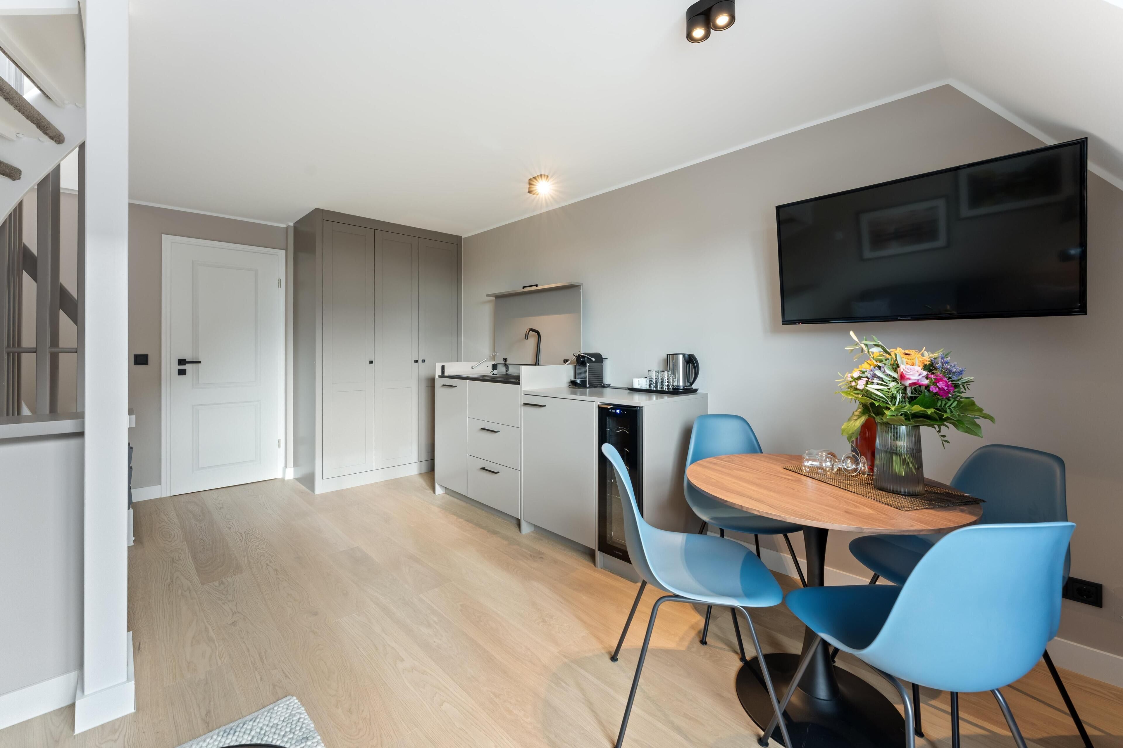 Una cocina moderna con armarios grises, lavavajillas integrado y un comedor con mesa de madera y sillas azules.