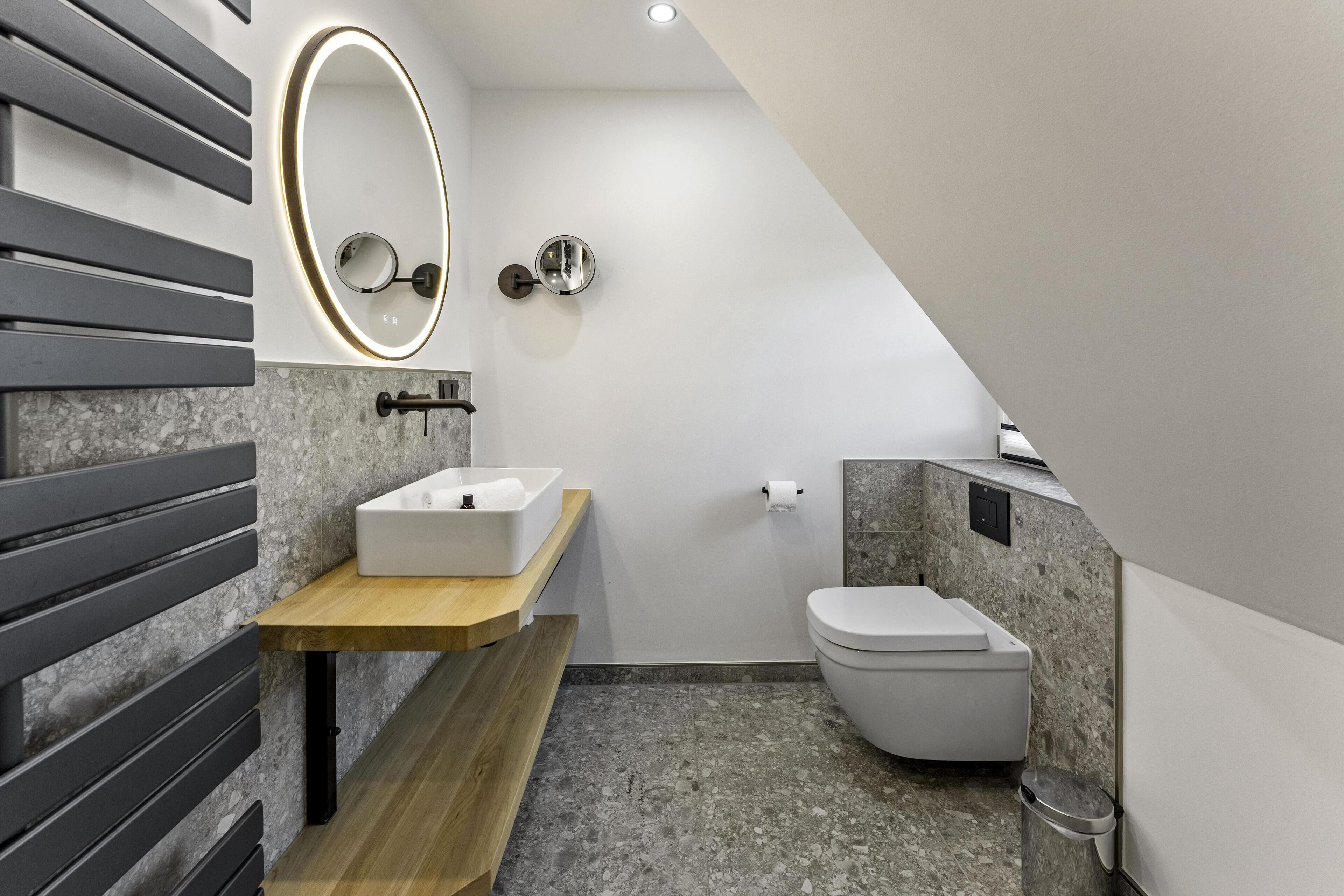A modern bathroom with a wooden vanity, a white toilet, and a wall-mounted mirror.