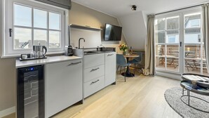 A modern kitchen with a built-in dishwasher, a flat-screen TV, and a dining area with a table and chairs. - Dependance Windrose 274 (Wenningstedt-Braderup (Sylt))