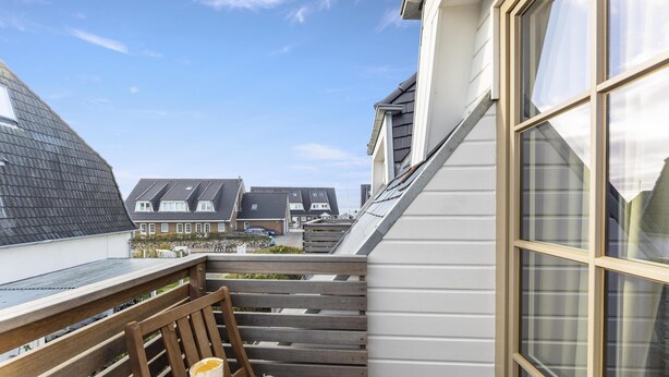 A balcony with a table and chairs, overlooking a residential area with houses. - Dependance Windrose 274 (Wenningstedt-Braderup (Sylt))
