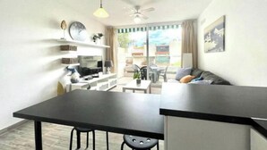 A compact living space with a dining area, a sofa, a TV, and a balcony with a view. - Apartment with pool south of Tenerife (CN)