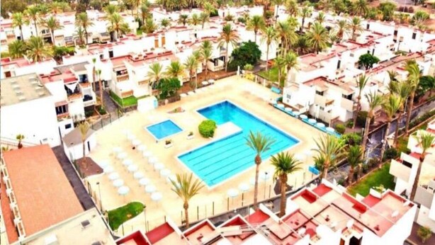 A residential area with a large swimming pool surrounded by palm trees and white buildings. - Apartment with pool south of Tenerife (CN)