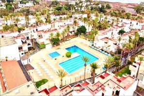 Ett bostadsområde med en stor swimmingpool omgiven av palmer och vita byggnader.