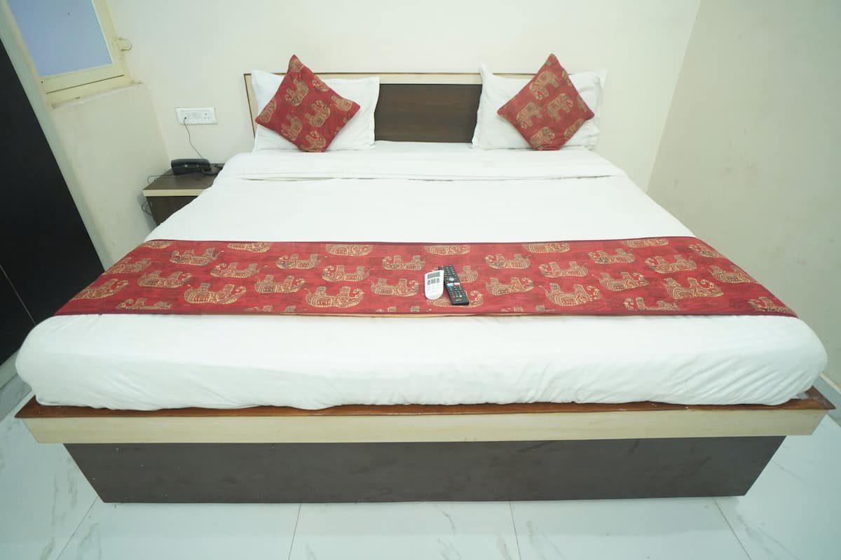 Ein Bett mit einer rot gemusterten Tagesdecke, weißen Kissen und einer Fernbedienung darauf.