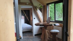 A cozy room with a bed, a wooden table, and a window with a view of greenery. - La linoterie Sauna privatif (Colembert)