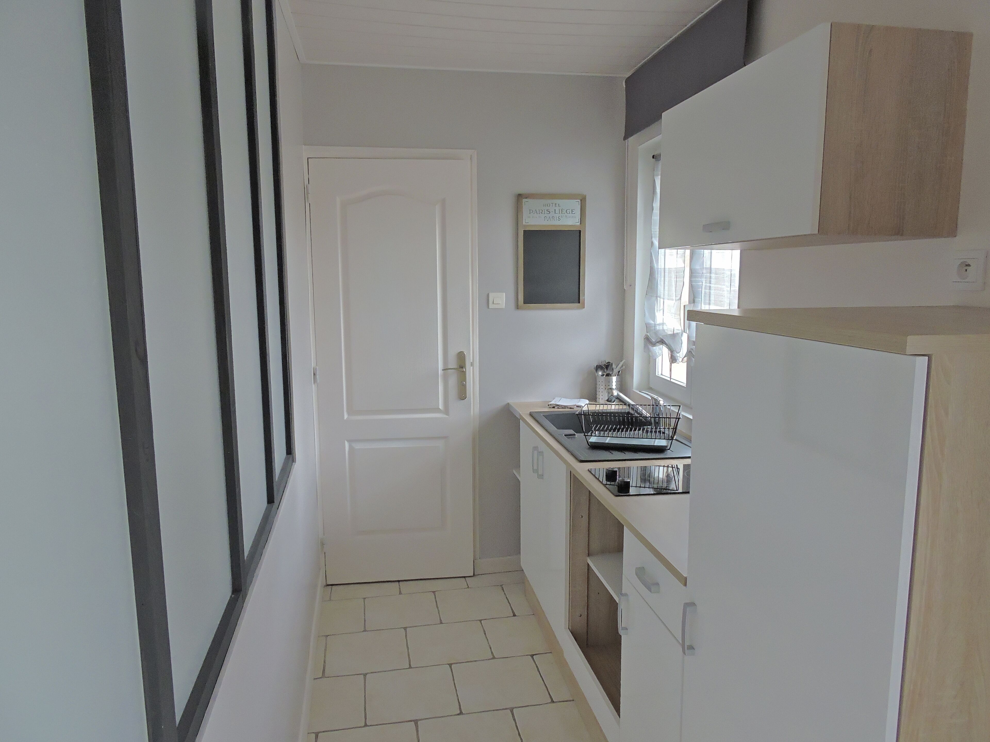Une cuisine étroite avec des meubles blancs, une cuisinière encastrée et une fenêtre avec des rideaux.