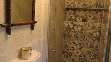 Un baño con ducha, un lavabo con taza y un espejo.