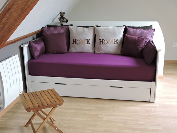 A white sofa with purple cushions and two pillows with "HOME" text, a small wooden stool, and a radiator. - La linoterie Sauna privatif (Colembert)