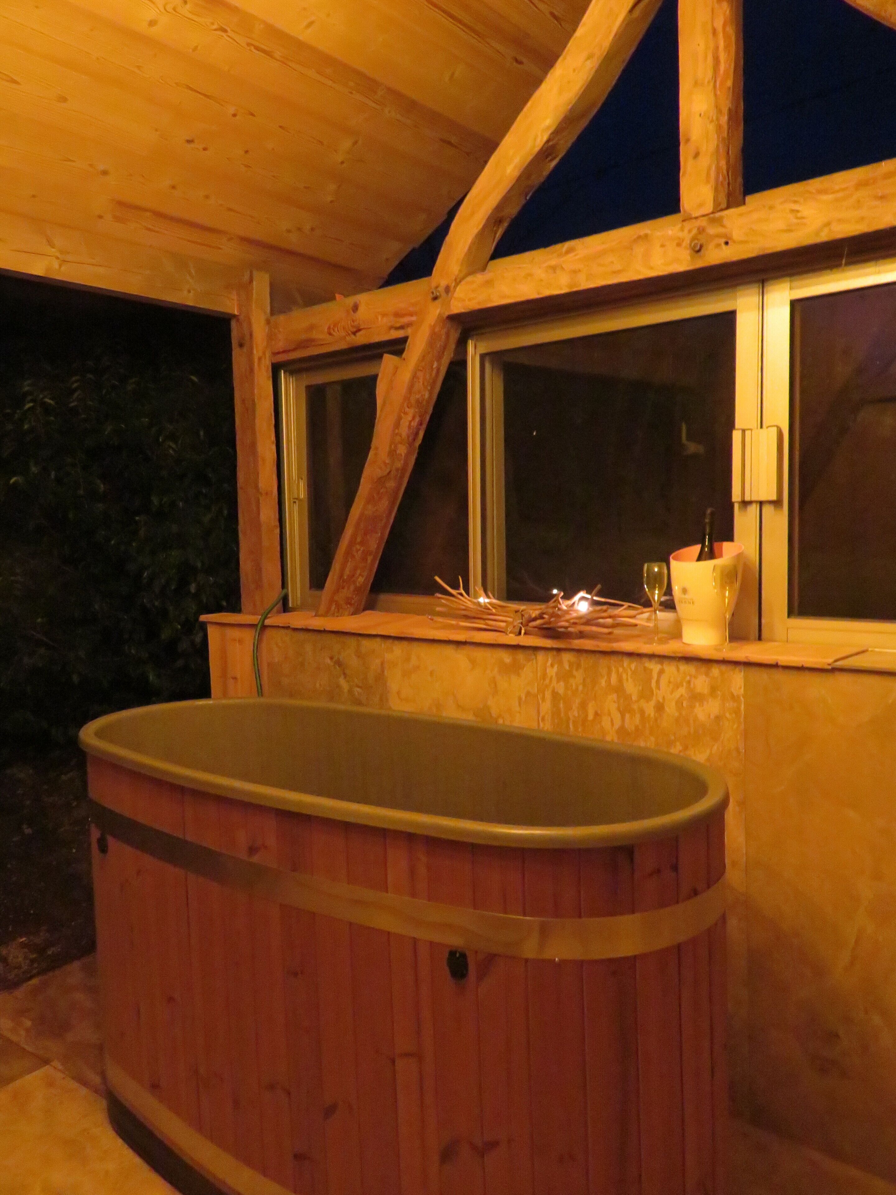 Un bain à remous en bois, situé dans une pièce dotée de grandes fenêtres et d’un plafond en bois.