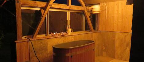 A wooden structure with a window, a hot tub, and hanging light bulbs.