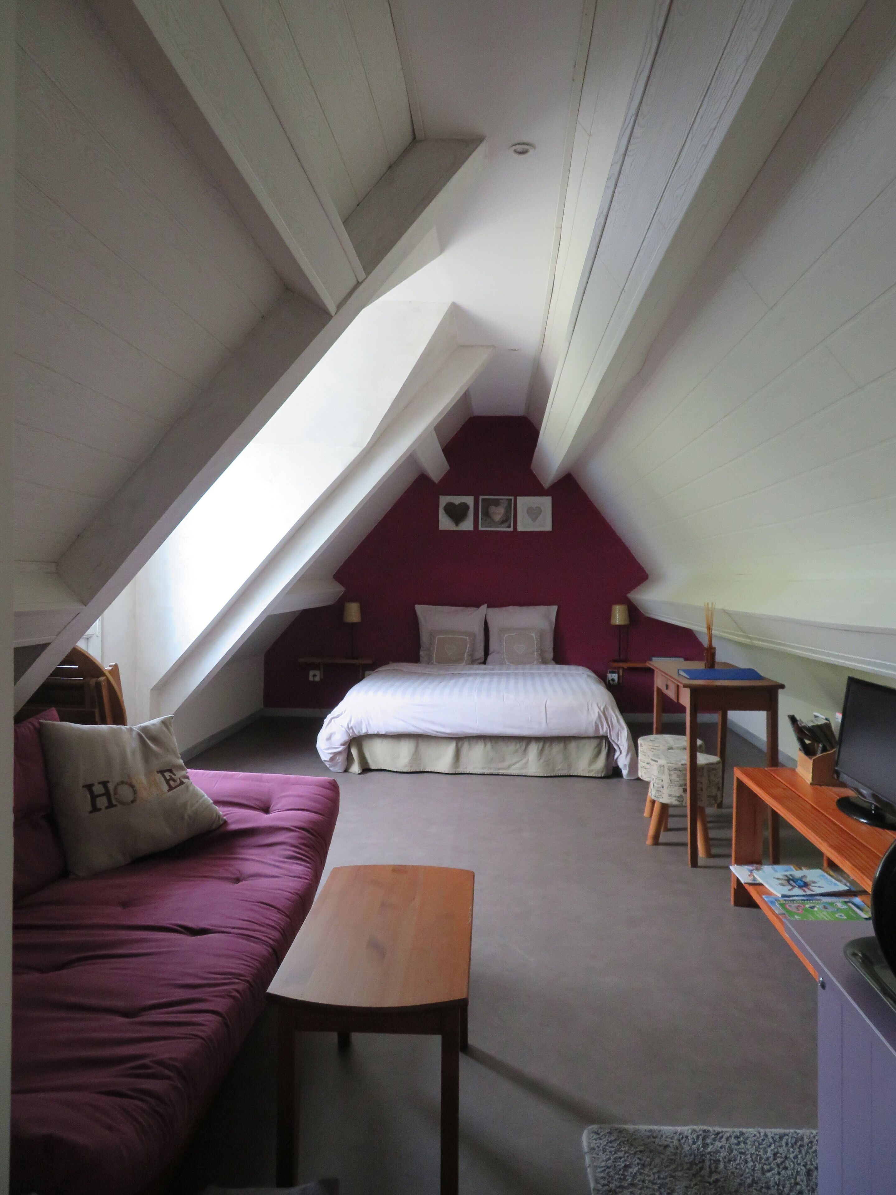 A small, cozy attic bedroom with a sloped ceiling, a bed, a sofa, and a desk.