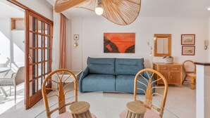 Ein Wohnzimmer mit einem blauen Sofa, Korbstühlen, einem Glastisch, einem Korbmöbel und einer großen, gewebten Deckenleuchte.