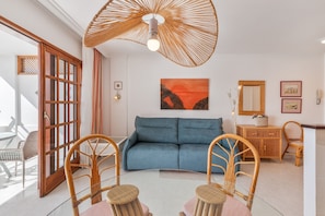 Ein Wohnzimmer mit einem blauen Sofa, Korbstühlen, einem Glastisch, einem Korbmöbel und einer großen, gewebten Deckenleuchte.