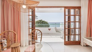 Ein Zimmer mit Glastisch, Korbstühlen, Sonnenschirm aus Korbgeflecht und Meerblick durch eine Glastür.