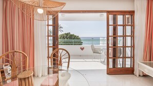 Et værelse med et glasbord, fletstole, en parasol af flet og havudsigt, samt en balkon med gelænder.