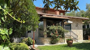 A stone house with a tiled roof, a stone staircase, and a well-maintained garden with a lawn and potted plants. - Villa Miramì (Saturnia)