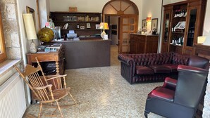 A cozy living room with a leather sofa, a wooden rocking chair, and a coffee table. There is a bookshelf filled with books and a wooden cabinet with wine bottles. - Villa Miramì (Saturnia)