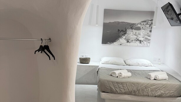A minimalist bedroom with a bed, a hanging light fixture, and a wall-mounted picture. - Fira Heart Studios (Santorini)