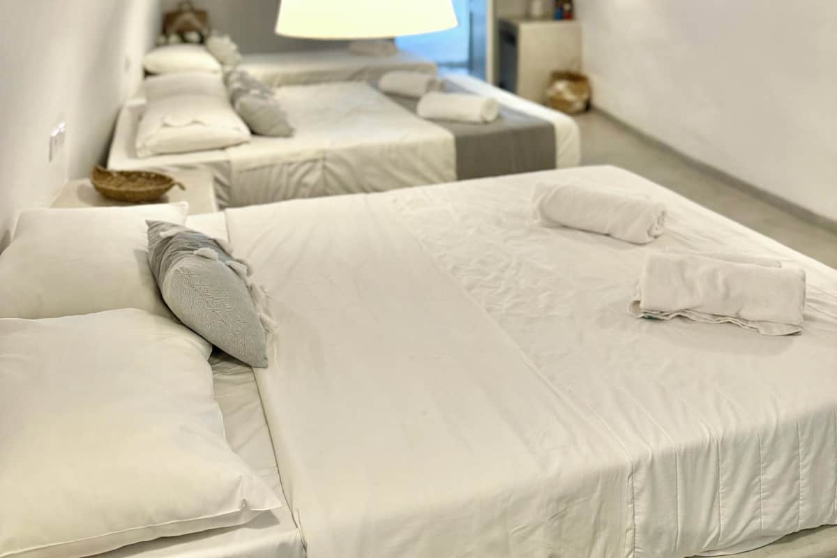 Een moderne, witte slaapkamer met twee bedden, een grote hanglamp en uitzicht naar buiten.