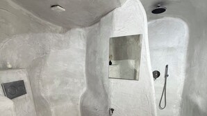 A bathroom with a white toilet, a shower with a handheld showerhead, and a small mirror. - Fira Heart Studios (Santorini)