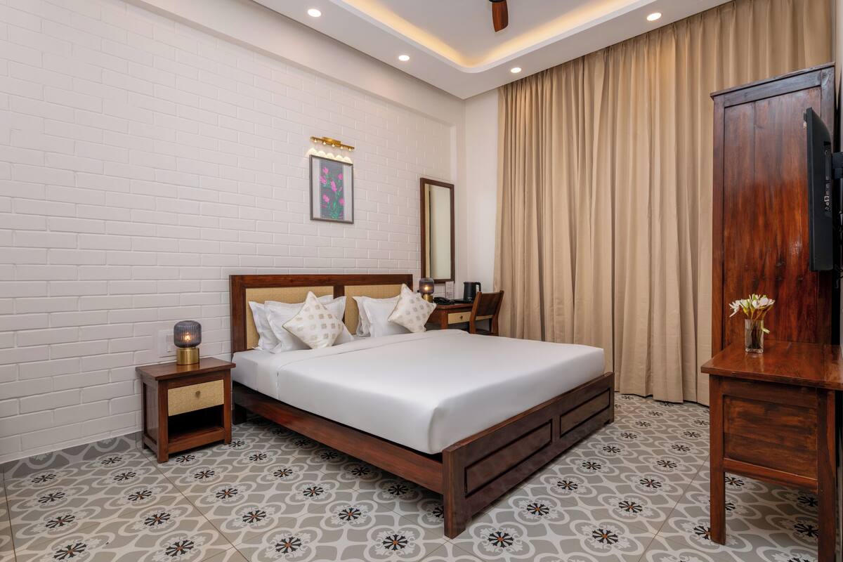 A hotel room with a wooden bed, a nightstand with a lamp, a mirror, and a television on a wooden stand.