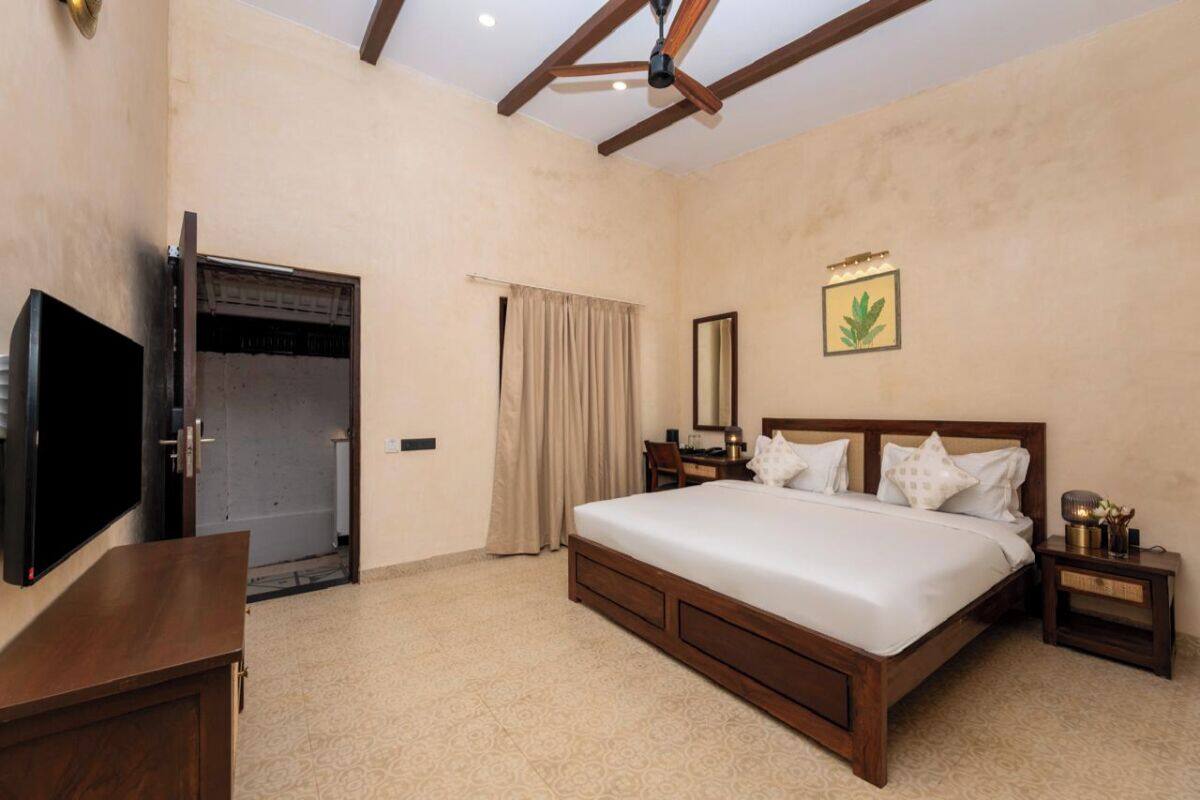A bedroom with a large bed, wooden headboard, bedside tables, a TV, and a ceiling fan.