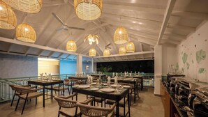 An indoor dining area with wicker furniture and hanging light fixtures. Tables are set with plates and glasses. - Yellowstone Resort Arambol (Arambol)