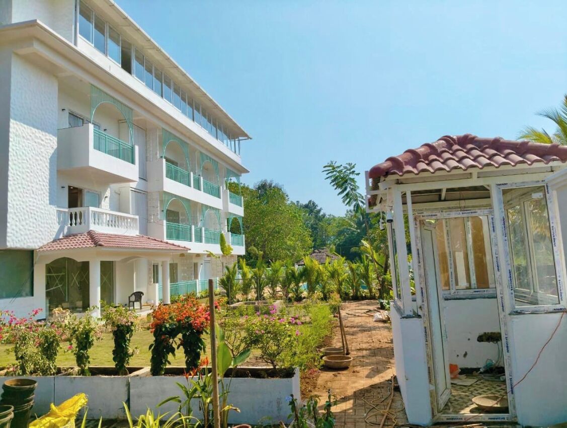 A multi-story building with balconies, a covered outdoor seating area, and a garden with various plants and flowers.
