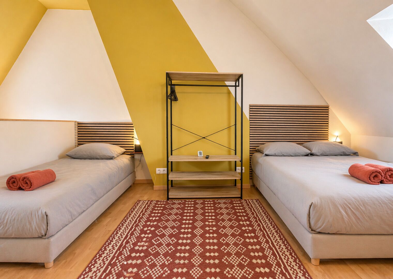 A triangular room with two beds, a central shelf, and a patterned rug.