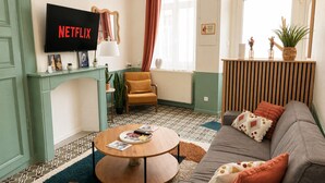 Una sala de estar con televisor, sofá, sillón, una mesa redonda de centro y piso con diseño.