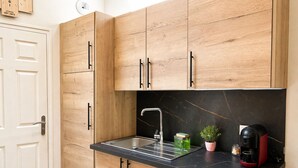 Una cocina compacta con armarios de madera, encimera negra, pileta de acero inoxidable y cafetera.