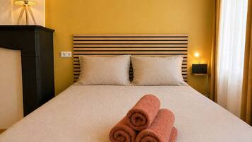 A hotel room with a bed, two pillows, a lamp, and a rolled towel on the bed.