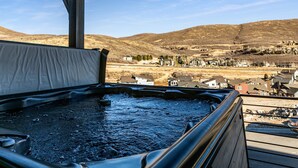Ein Whirlpool auf einer Holzdiele mit Blick auf eine kleine Stadt und Hügel im Hintergrund.