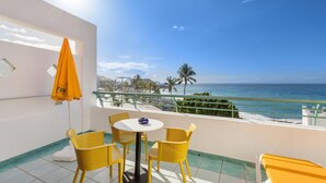 A balcony with yellow chairs, a table, and a sun umbrella overlooking a beach.