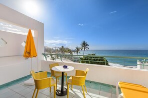 Een balkon met gele stoelen, een tafel en een parasol, met uitzicht op een strand.