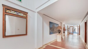 A hallway with a large mirror, a painting, and a lamp on a pedestal.