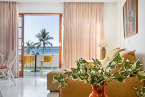 Une chambre d’hôtel avec un lit, un vase contenant des feuilles vertes, une vue sur l’océan et un coin repas avec une table et des chaises.